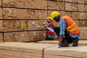 African workers man engineering walking and inspecting with working suite dress and hand glove in timber wood warehouse. Concept of smart industry worker operating. Wood factories produce wood palate. photo