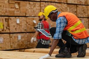 African workers man engineering walking and inspecting with working suite dress and hand glove in timber wood warehouse. Concept of smart industry worker operating. Wood factories produce wood palate. photo