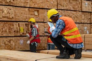 African workers man engineering walking and inspecting with working suite dress and hand glove in timber wood warehouse. Concept of smart industry worker operating. Wood factories produce wood palate. photo