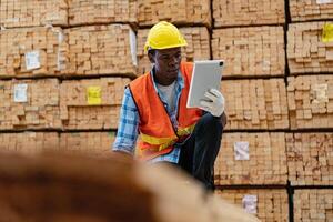 African workers man engineering walking and inspecting with working suite dress and hand glove in timber wood warehouse. Concept of smart industry worker operating. Wood factories produce wood palate. photo