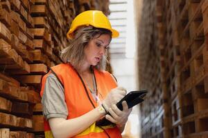 woman worker carpenter wearing safety uniform and hard hat working and checking the quality of wooden products at workshop manufacturing. man and woman workers wood in dark warehouse industry. photo