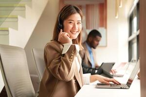 Asian operator working in office. Young friendly operator woman agent with headsets working in a call centre. photo