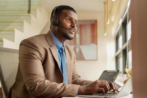 Customer Support Call Center Operator Or Receptionist. customer service and man consultant talking while doing a consultation online. African operator male telemarketing agent on a laptop in office photo