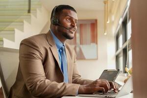 Customer Support Call Center Operator Or Receptionist. customer service and man consultant talking while doing a consultation online. African operator male telemarketing agent on a laptop in office photo