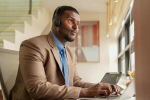 Customer Support Call Center Operator Or Receptionist. customer service and man consultant talking while doing a consultation online. African operator male telemarketing agent on a laptop in office photo