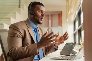 Customer Support Call Center Operator Or Receptionist. customer service and man consultant talking while doing a consultation online. African operator male telemarketing agent on a laptop in office photo