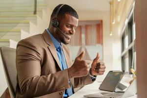 cliente apoyo llamada centrar operador o recepcionista. cliente Servicio y hombre consultor hablando mientras haciendo un consulta en línea. africano operador masculino telemarketing agente en un ordenador portátil en oficina foto