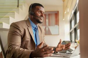 cliente apoyo llamada centrar operador o recepcionista. cliente Servicio y hombre consultor hablando mientras haciendo un consulta en línea. africano operador masculino telemarketing agente en un ordenador portátil en oficina foto