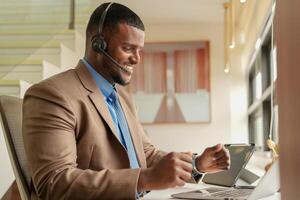 cliente apoyo llamada centrar operador o recepcionista. cliente Servicio y hombre consultor hablando mientras haciendo un consulta en línea. africano operador masculino telemarketing agente en un ordenador portátil en oficina foto