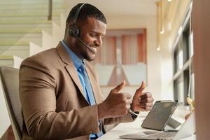 cliente apoyo llamada centrar operador o recepcionista. cliente Servicio y hombre consultor hablando mientras haciendo un consulta en línea. africano operador masculino telemarketing agente en un ordenador portátil en oficina foto