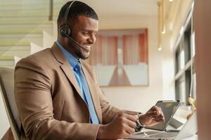 Customer Support Call Center Operator Or Receptionist. customer service and man consultant talking while doing a consultation online. African operator male telemarketing agent on a laptop in office photo