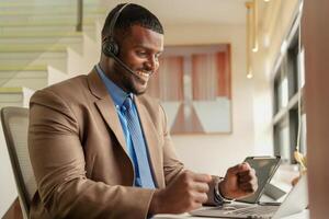 cliente apoyo llamada centrar operador o recepcionista. cliente Servicio y hombre consultor hablando mientras haciendo un consulta en línea. africano operador masculino telemarketing agente en un ordenador portátil en oficina foto