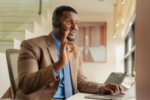 Customer Support Call Center Operator Or Receptionist. customer service and man consultant talking while doing a consultation online. African operator male telemarketing agent on a laptop in office photo