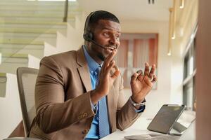 cliente apoyo llamada centrar operador o recepcionista. cliente Servicio y hombre consultor hablando mientras haciendo un consulta en línea. africano operador masculino telemarketing agente en un ordenador portátil en oficina foto