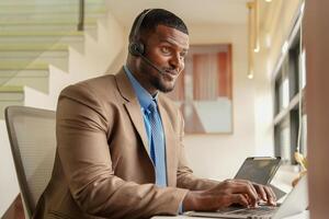 Customer Support Call Center Operator Or Receptionist. customer service and man consultant talking while doing a consultation online. African operator male telemarketing agent on a laptop in office photo