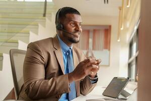 Customer Support Call Center Operator Or Receptionist. customer service and man consultant talking while doing a consultation online. African operator male telemarketing agent on a laptop in office photo