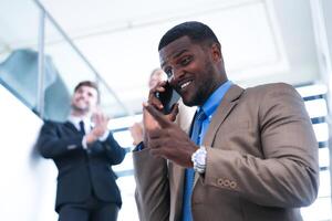 inteligente negro empresario acecho móvil teléfono. calvo adulto hombre vistiendo formal tener puesto. pensativo afroamericano empresario en un perfectamente a la medida traje en pie en escalera en oficina. foto