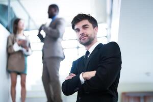 business people and office concept. happy smiling businessman in dark suit. Portrait of smiling mid adult businessman standing at corporate office. Businessman smiling with arms crossed in office. photo