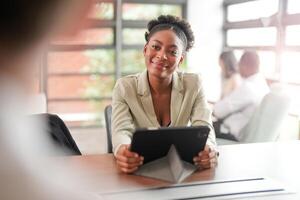 African black business woman using smartphone while working on laptop at office. Smiling mature african american businesswoman looking up while working on phone. Successful woman entrepreneur. photo