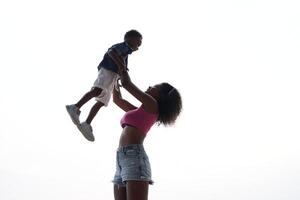 mezclado carrera africano y asiático madre y chico es jugando a el al aire libre área. sonriente contento familia tener divertido corriendo en el playa. retrato de mamá y niño estilo de vida con un único peinado. foto