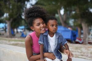 mezclado carrera africano y asiático madre y chico es jugando a el al aire libre área. sonriente contento familia tener divertido corriendo en el playa. retrato de mamá y niño estilo de vida con un único peinado. foto