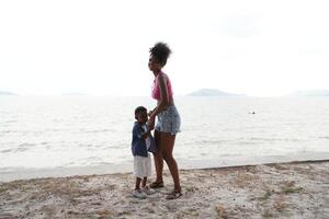 Mixed race African and Asian mother and boy is playing at the outdoor area. smiling happy family have fun running on the beach. portrait of mom and kid lifestyle with a unique hairstyle. photo