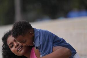 mezclado carrera africano y asiático madre y chico es jugando a el al aire libre área. sonriente contento familia tener divertido corriendo en el playa. retrato de mamá y niño estilo de vida con un único peinado. foto