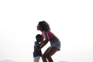 mezclado carrera africano y asiático madre y chico es jugando a el al aire libre área. sonriente contento familia tener divertido corriendo en el playa. retrato de mamá y niño estilo de vida con un único peinado. foto