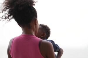 mezclado carrera africano y asiático madre y chico es jugando a el al aire libre área. sonriente contento familia tener divertido corriendo en el playa. retrato de mamá y niño estilo de vida con un único peinado. foto