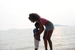 Mixed race African and Asian mother and boy is playing at the outdoor area. smiling happy family have fun running on the beach. portrait of mom and kid lifestyle with a unique hairstyle. photo