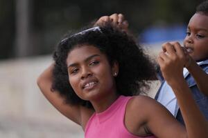 mezclado carrera africano y asiático madre y chico es jugando a el al aire libre área. sonriente contento familia tener divertido corriendo en el playa. retrato de mamá y niño estilo de vida con un único peinado. foto