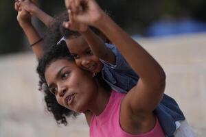 mezclado carrera africano y asiático madre y chico es jugando a el al aire libre área. sonriente contento familia tener divertido corriendo en el playa. retrato de mamá y niño estilo de vida con un único peinado. foto