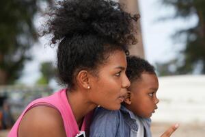 Mixed race African and Asian mother and boy is playing at the outdoor area. smiling happy family have fun running on the beach. portrait of mom and kid lifestyle with a unique hairstyle. photo