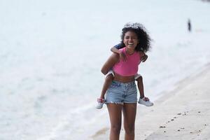 mezclado carrera africano y asiático madre y chico es jugando a el al aire libre área. sonriente contento familia tener divertido corriendo en el playa. retrato de mamá y niño estilo de vida con un único peinado. foto