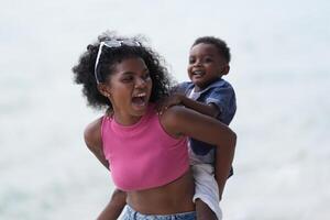 mezclado carrera africano y asiático madre y chico es jugando a el al aire libre área. sonriente contento familia tener divertido corriendo en el playa. retrato de mamá y niño estilo de vida con un único peinado. foto