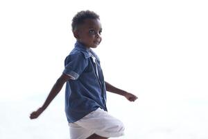 mezclado carrera africano y asiático chico es jugando a el al aire libre área. sonriente contento chico tiene divertido corriendo en el playa. retrato de chico estilo de vida con un único peinado. foto