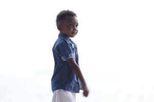 mezclado carrera africano y asiático chico es jugando a el al aire libre área. sonriente contento chico tiene divertido corriendo en el playa. retrato de chico estilo de vida con un único peinado. foto