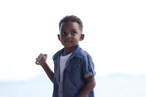 mezclado carrera africano y asiático chico es jugando a el al aire libre área. sonriente contento chico tiene divertido corriendo en el playa. retrato de chico estilo de vida con un único peinado. foto