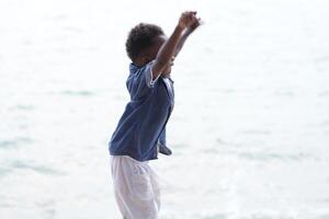 Mixed race African and Asian boy is playing at the outdoor area. smiling happy boy has fun running on the beach. portrait of boy lifestyle with a unique hairstyle. photo