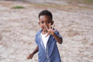 mezclado carrera africano y asiático chico es jugando a el al aire libre área. sonriente contento chico tiene divertido corriendo en el playa. retrato de chico estilo de vida con un único peinado. foto