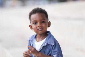 mezclado carrera africano y asiático chico es jugando a el al aire libre área. sonriente contento chico tiene divertido corriendo en el playa. retrato de chico estilo de vida con un único peinado. foto