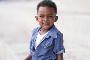 mezclado carrera africano y asiático chico es jugando a el al aire libre área. sonriente contento chico tiene divertido corriendo en el playa. retrato de chico estilo de vida con un único peinado. foto