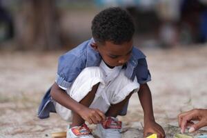 mezclado carrera africano y asiático chico es jugando a el al aire libre área. sonriente contento chico tiene divertido corriendo en el playa. retrato de chico estilo de vida con un único peinado. foto