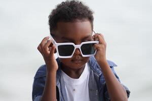 mezclado carrera africano y asiático chico es jugando a el al aire libre área. sonriente contento chico tiene divertido corriendo en el playa. retrato de chico estilo de vida con un único peinado. foto