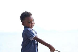 mezclado carrera africano y asiático chico es jugando a el al aire libre área. sonriente contento chico tiene divertido corriendo en el playa. retrato de chico estilo de vida con un único peinado. foto