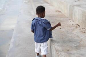 mezclado carrera africano y asiático chico es jugando a el al aire libre área. sonriente contento chico tiene divertido corriendo en el playa. retrato de chico estilo de vida con un único peinado. foto