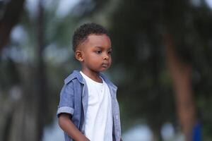 mezclado carrera africano y asiático chico es jugando a el al aire libre área. sonriente contento chico tiene divertido corriendo en el playa. retrato de chico estilo de vida con un único peinado. foto