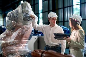 Sales manager and factory owner in suits negotiating selling robots used in the factory. Business engineers meeting and checking new machine robot. Workers walking at warehouse welding machine. photo