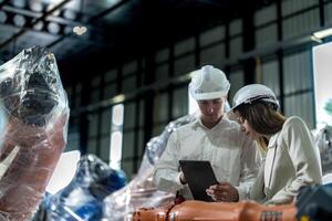 Business engineers meet and check control heavy machine robot arm. Diverse Team of Industrial Robotics Engineers Gathered Around machine. Professional Machinery Operator Use Industrial Digital Tablet. photo