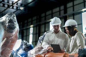 Factory engineers inspecting on machine with smart tablet. Worker works at machine robot arm. The welding machine with a remote system in an industrial factory. Artificial intelligence concept. photo